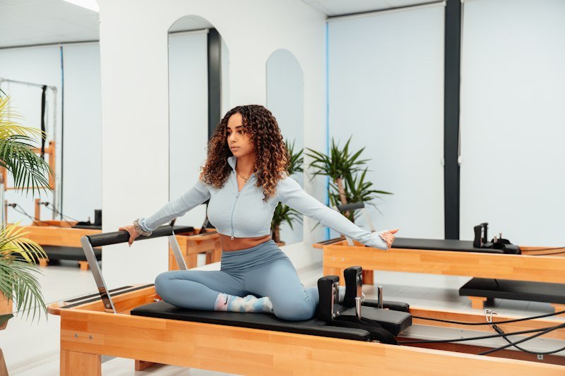 A member seated on a reformer with arms stretched wide, holding the straps